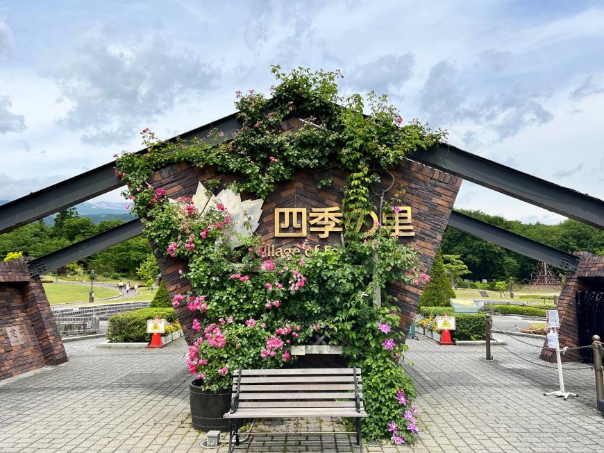 「四季の里」と書かれ壁側ににバラの花が咲いているアーチの入り口付近の写真