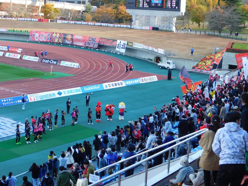 アスルクラロ沼津の選手とキャラクター達が観覧スタンド側に立ち、多くの観戦者達と賑わっている様子の写真