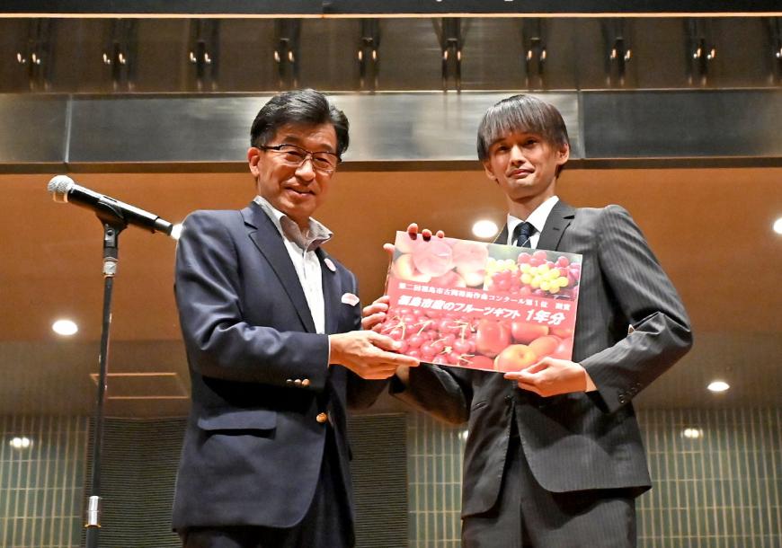 第一位を受賞した萩原友輔さんと市長が果物が写った副賞の福島市産フルーツギフトのパネルを一緒に持っている写真