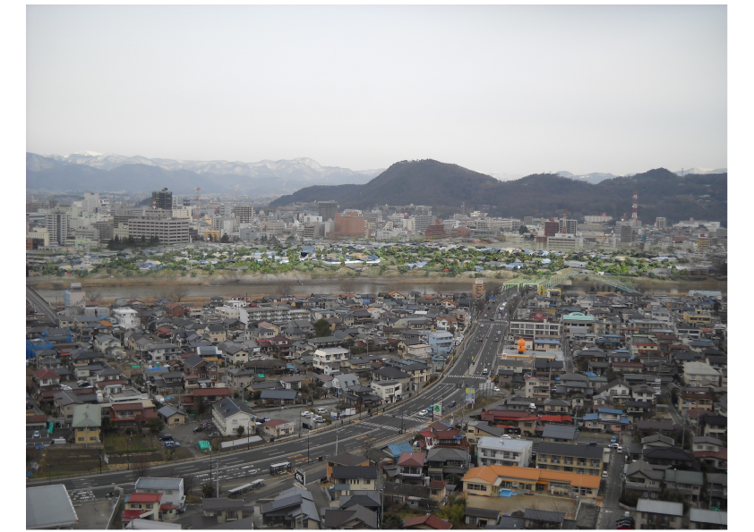 奥に山が見え、住宅街の中央に大きな道路が通っている弁天山から見た市街地の写真