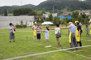 弓を構えた子供たちが横一列に並び、案内人の方が弓矢の飛ばしかたをサポートしている写真