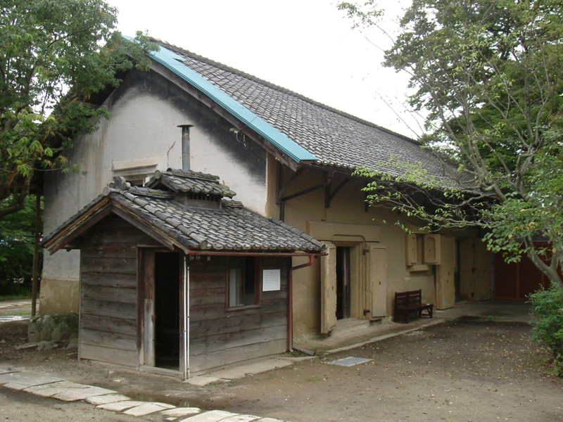 木造の小さな小屋のような建物の奥に建っている横長で瓦屋根をした十間蔵の写真