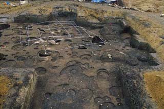 地面に複数の丸い大きな穴が掘られた跡が見られる掘立柱建物跡の写真