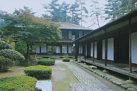 手前右側に縁側のある平屋建ての家、左側に整備された植栽のある庭園、奥に2階建ての家が建っている元客自軒 旧東棟及び旧北棟の写真