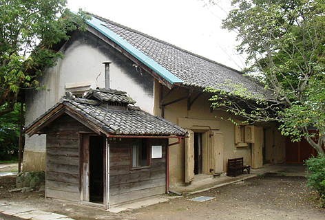 木造の小さな小屋のような建物の奥に建っている横長で瓦屋根をした十間蔵の写真