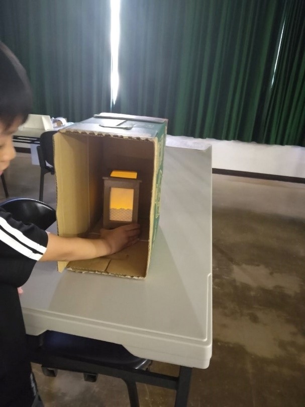 横にした段ボールの中に行灯を入れて明かりを付ける男の子を撮影した写真