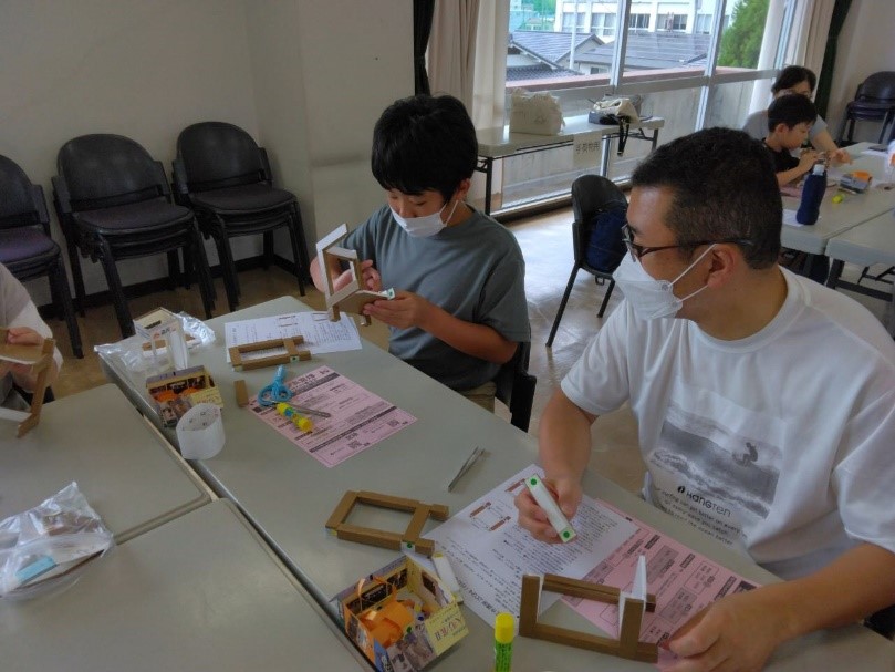 男の子が行灯を作っている様子を横からじっと見ている男性の写真