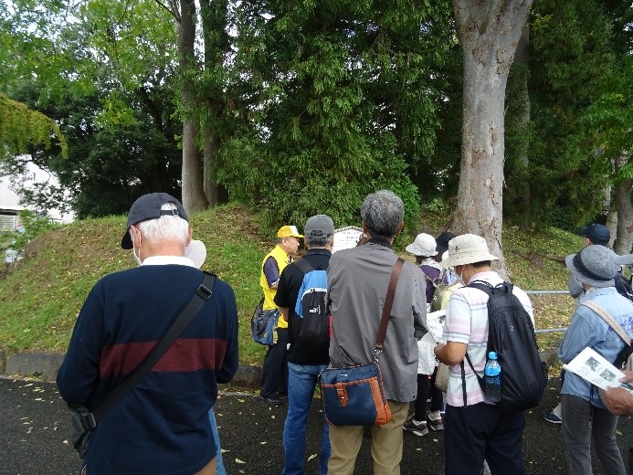 土の盛り上がった福島城土塁の看板の前で資料と見比べる受講者たちを撮影した写真