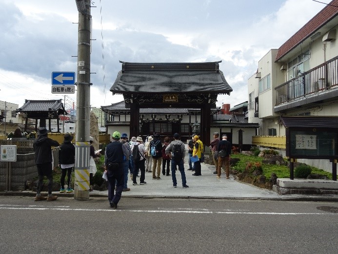 2階建ての建物と同じ高さのある康善寺の門を下から眺めている受講者たちを撮影した写真