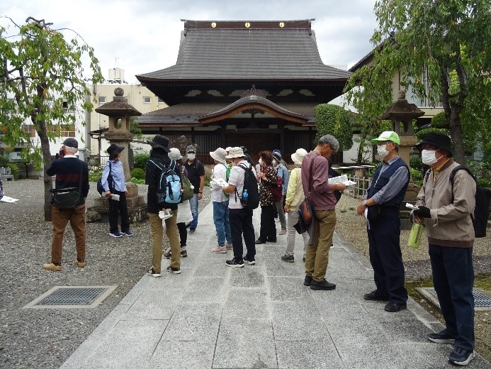 到岸寺の柳の木が生える境内で資料を読む受講者たちを撮影した写真