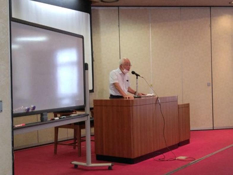 講師の男性が壇上にあるマイクで受講者に説明をしている写真