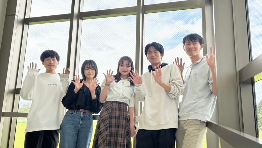 福島県立医科大学アカペラサークル阿修羅のメンバー5名が笑顔で手を振って写っている写真