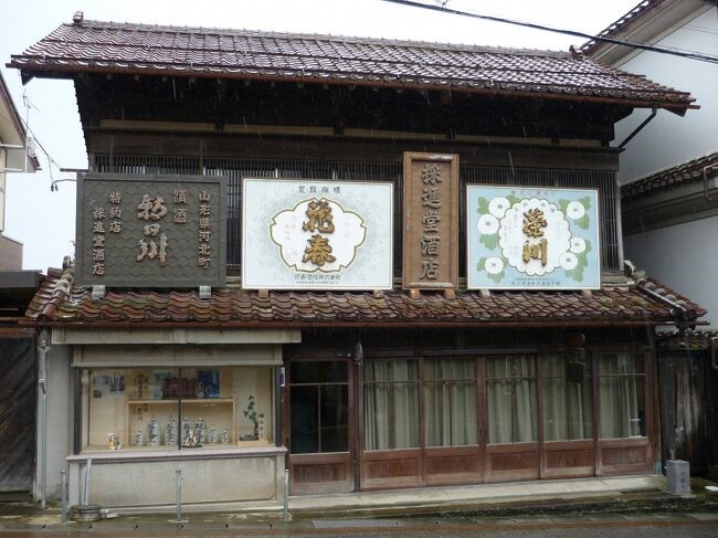 お酒の銘柄が書かれた看板が屋根の上に並ぶ旧採進堂酒店を正面から撮影している写真