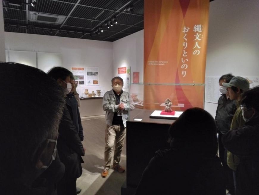 目玉である展示品を見ながら説明をする講師と受講者たちを撮影した写真