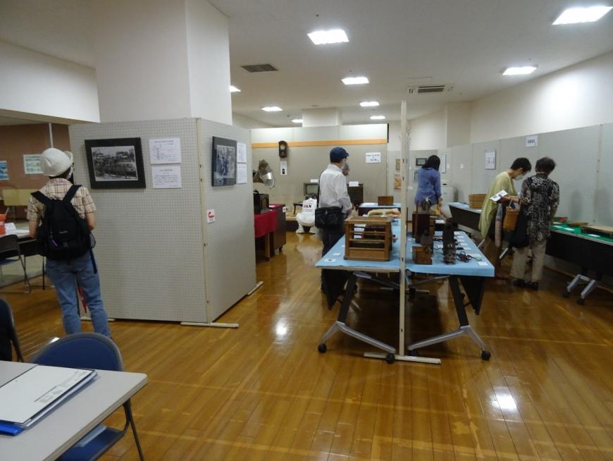 台の上に展示されている昔の暮らしの道具を鑑賞している来場者たちの写真