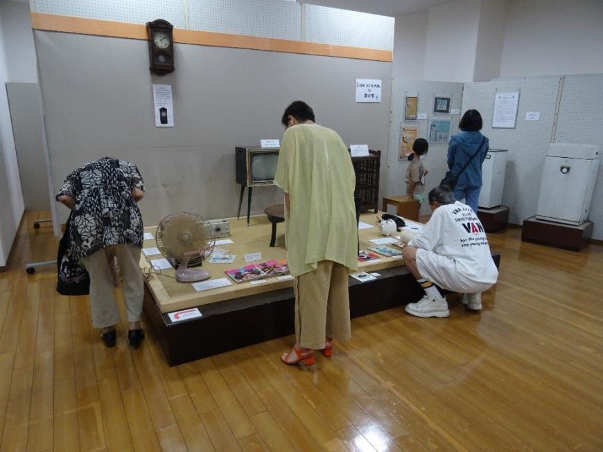 小上がりになった場所に展示されている昔のテレビは扇風機、時計などを鑑賞している来場者たちを後方から写した写真