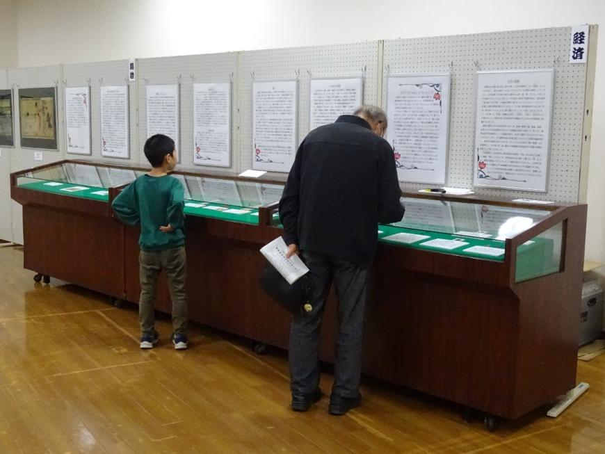 男の子が壁に展示されている資料を、男性がケースの中に入った資料を見ている写真
