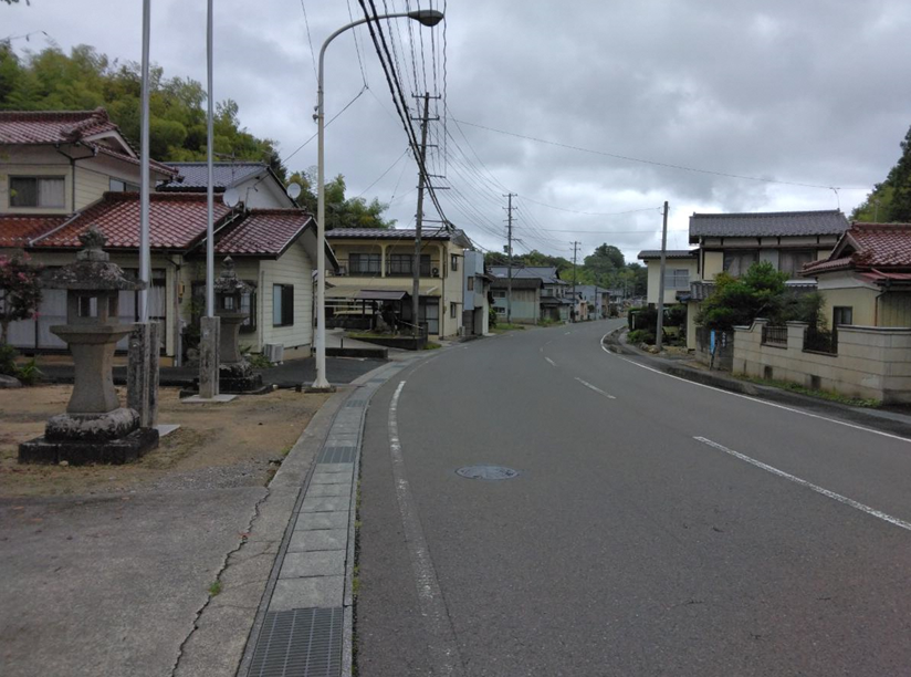 カーブになった道路の両側に住宅が立ち並び、左側には石灯籠が見える現在の清水町の写真