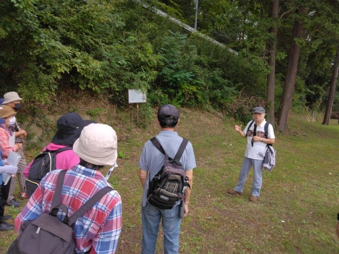 信夫山児童公園内にある説明板の横でマイクを持って説明をする講師を撮影した写真