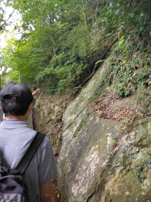 弁慶の足あと石がある苔の生えた岸壁を見る受講者たちの写真