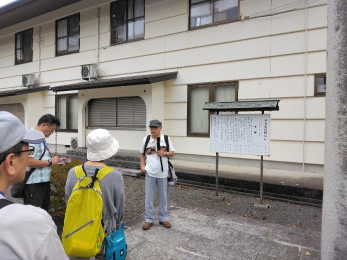 護國神社の看板前で受講者に説明をする講師を撮影した写真