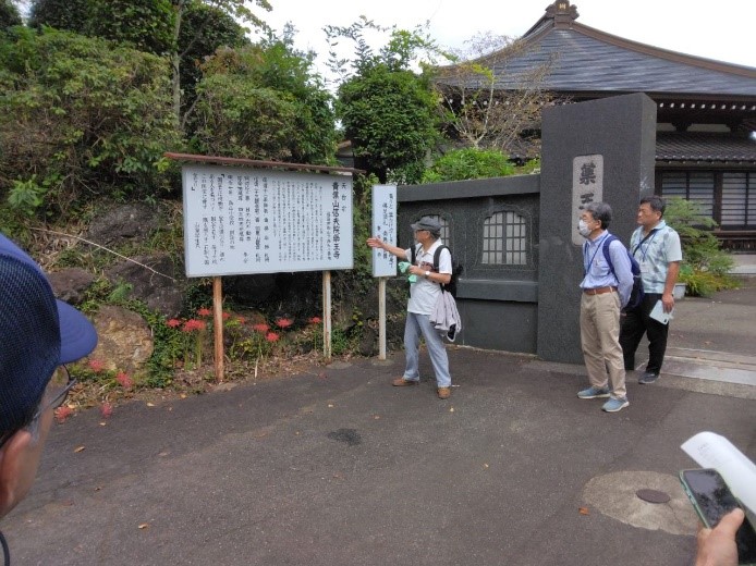 薬王寺と大きく彫られた表札の前にある説明板を読む受講者たちを撮影した写真
