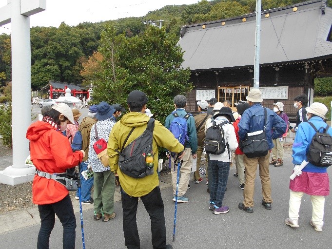 黒沼神社の鳥居の脇にあるヒサカキの木について説明する講師と話を聞く受講者たちを撮影した写真