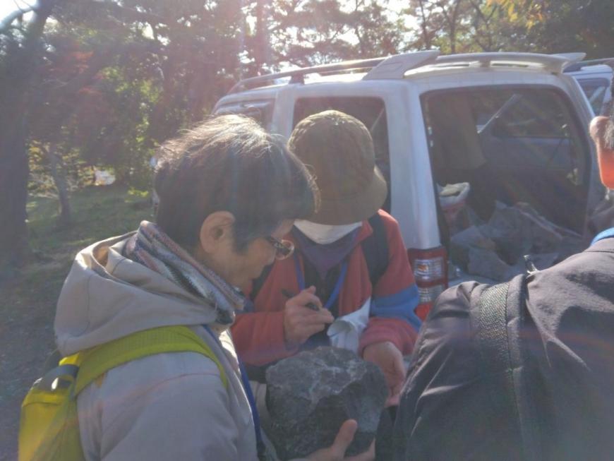 大きな岩石を両手で持ち観察している参加者たちの写真