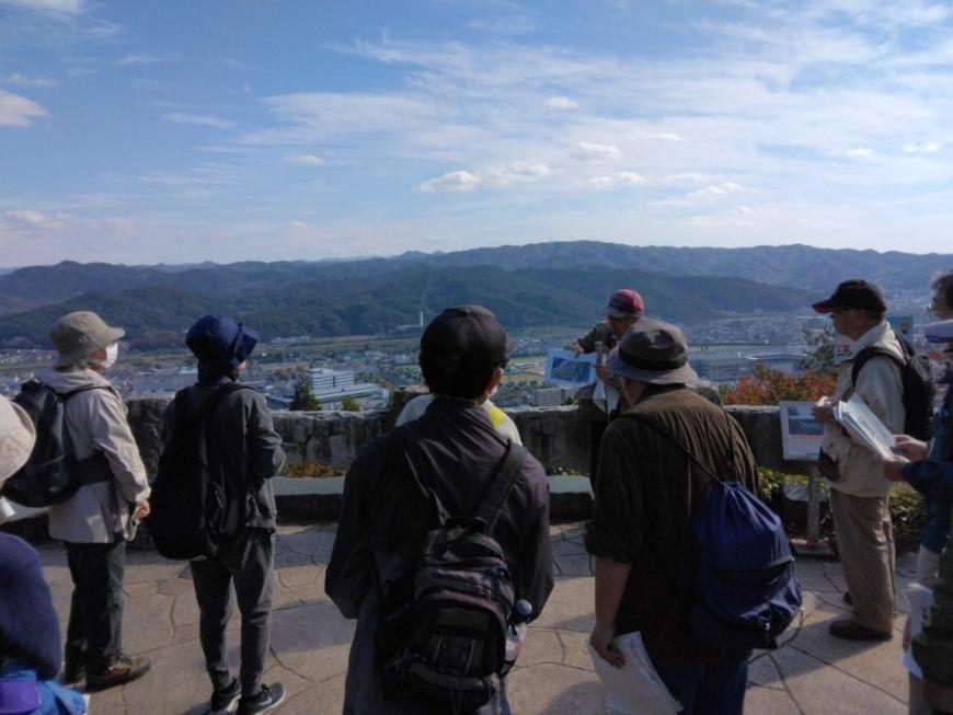 青空と街並みや向かいの山が全貌できる第二展望台で紙を使って説明する講師を撮影した写真