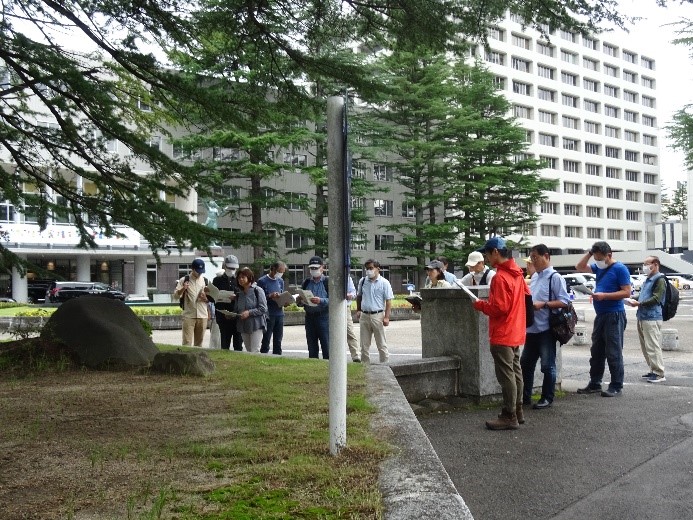 屋敷跡に置かれた大佛城阯碑を資料を見ながら観察する受講者たちを撮影した写真