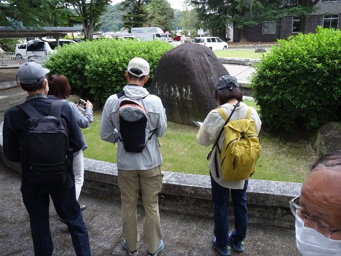 福島城址碑の前で撮影や資料にメモをする受講者たちの後ろ姿を撮影した写真