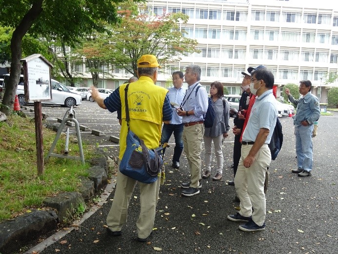 福島城土塁の説明板を読む受講者たちの隣で説明をしている講師を撮影した写真