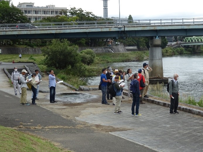 福島河岸の岸辺に集まり河川を眺める受講者たちの写真