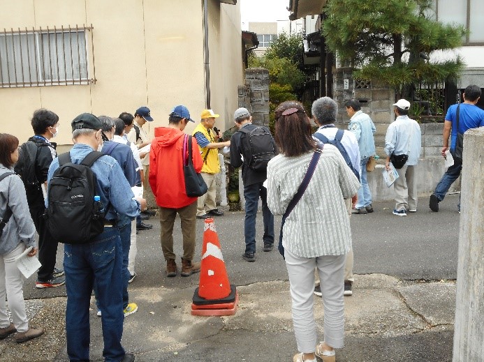 在宝院にある石碑の説明をする講師と話を聞く受講者たちを撮影した写真