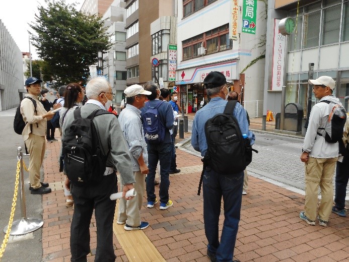 煉瓦通りにある古関裕而生誕の地記念碑を歩行者の邪魔にならないように遠くから見る受講者たちの写真