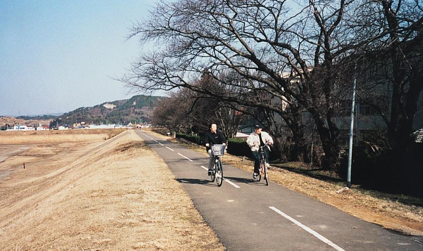 2名の方が堤防の上に整備されたサイクリングロードを自転車で走っている写真