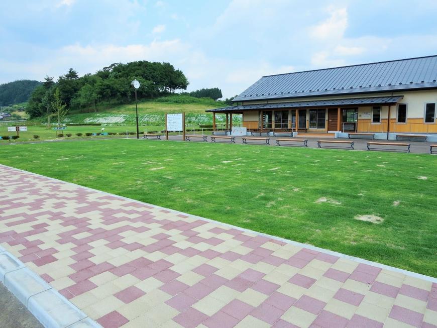 クリーム色とピンクのレンガが敷かれた歩道の奥に、整備された芝生、平屋建てのの建物が建っているNCVふくしまパークゴルフ場の写真