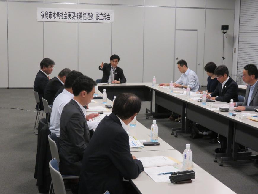 机がコの字に並べられ、着席し手元の資料を見ながら話をしている参加者と市長の写真