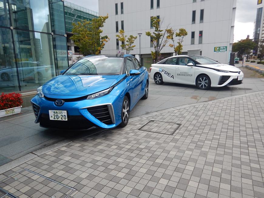 青い車体の燃料電池自動車と白い車体の燃料電池自動車が2台並んで展示されている写真