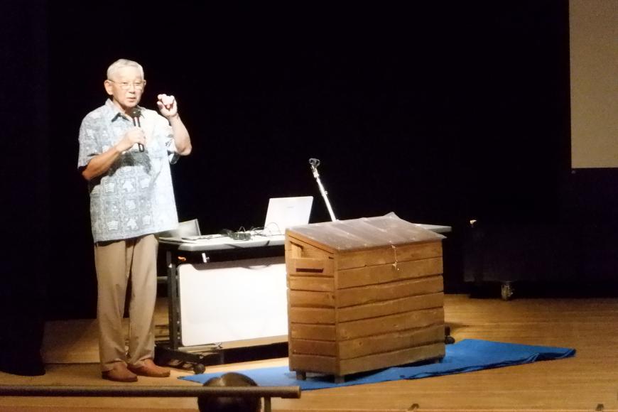 松本信夫先生が檀上横でマイクを持って話をしている様子の写真