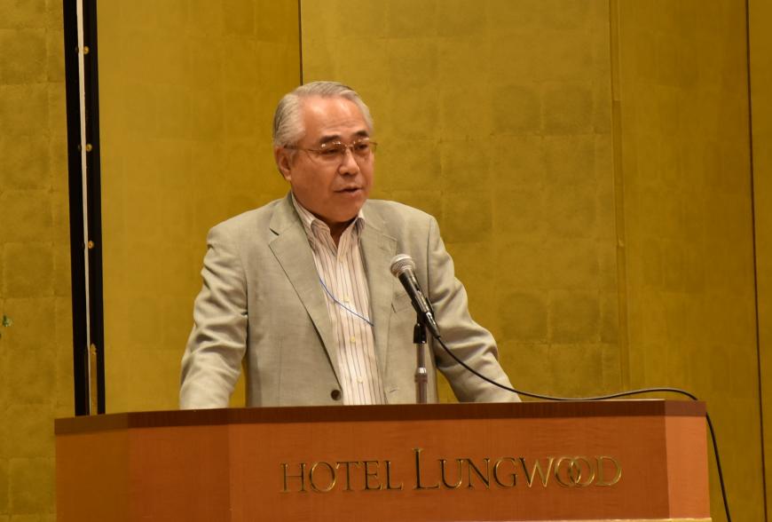 バックに金屏風がある演台に立ち佐藤文俊会長が挨拶をしている写真