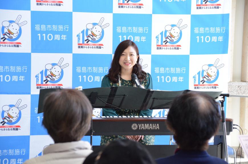 福島市制施行110周年のバックパネルの前に設置された電子ピアノの演奏席に座った星さんが笑顔で観客の方を見ている写真