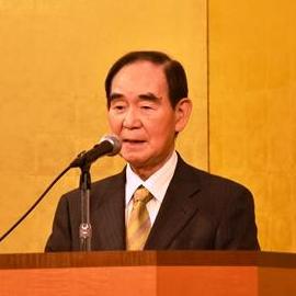 演台に置かれたマイクの前に立ち阿部孝夫会長が挨拶をしている写真