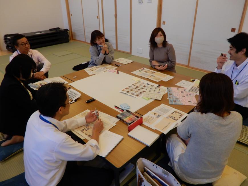 四角の大きめのテーブルの周りに8名の関係者の方々が座りながら話し合いをしている写真
