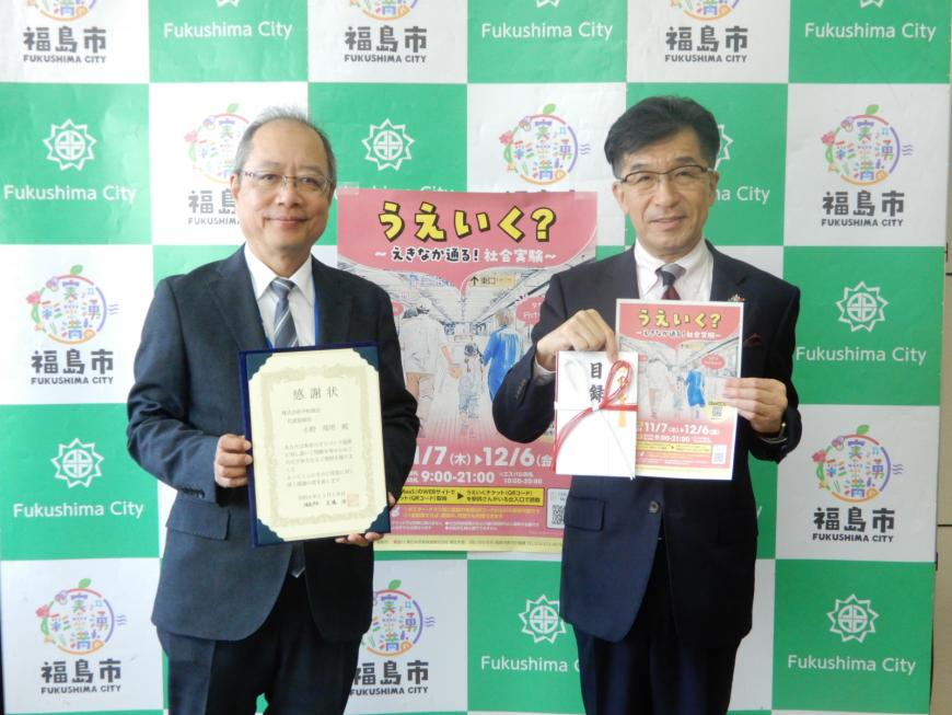 バックボードの前で市長が目録と「うえいく?」のチラシを持ち、株式会社中松商会の男性が感謝状を持ちながら2人並んで記念撮影をしている写真