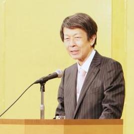 演台の上にグラスを置き、板野裕爾副会長が乾杯挨拶をしている写真