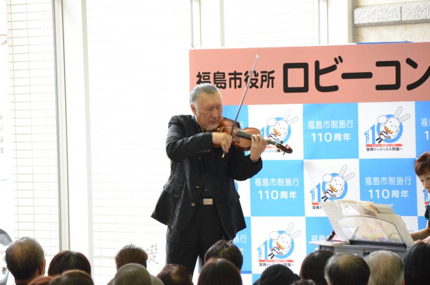 バックパネルの前で男性がヴァイオリンを演奏している写真