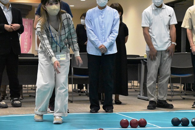女性がボールを投げているところを他の参加者が後ろで見守っているボッチャを体験するようすの写真