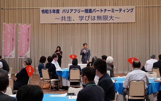 「令和5年度バリアフリー推進パートナーミーティング 共生、学びは無限大」と書かれた横断幕の下で木幡市長がマイクを持ち話しをしている様子の写真