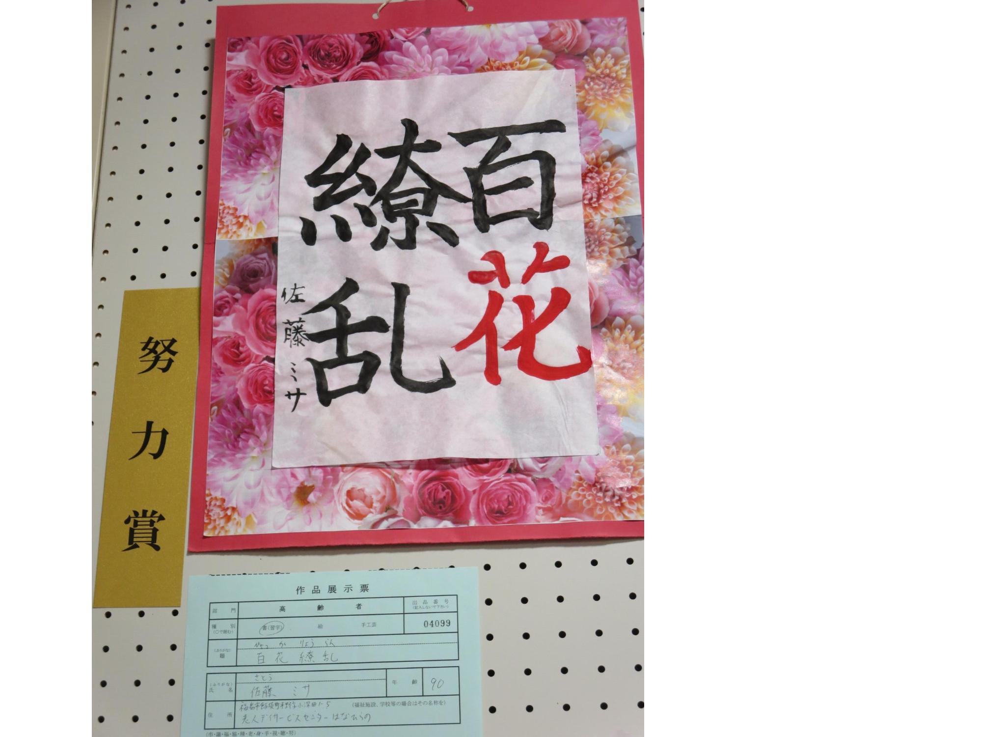 花柄の紙の上に「花」の文字だけ赤色で書いた「百花繚乱」と書かれた書が展示された努力賞受賞作品の写真